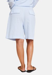 Lys blå linshorts med avslappet passform, med to baklommer og en ren søm. Brukt med svarte flip-flops.