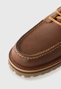Chaussure en cuir marron avec un bout rond, des coutures contrastantes et une semelle texturée. Présente des accents beiges et un design à lacets.