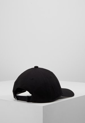 Sort justerbar baseballkasket, der hviler på en hvid overflade med hjørne, vist bagfra med en buet skygge vendt mod højre.