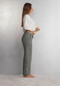 Grijze geruite broek met een trekkoord in de taille, gecombineerd met een witte longsleeve top. Zachte textuur zichtbaar, model zijwaarts weergegeven.
