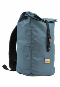 Mochila azul tipo roll-top fabricada con tejido duradero. Cuenta con correas ajustables, panel trasero texturizado y un parche de logo bordado. Diseño simple.