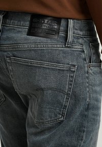 Denim jeans in een vervaagd donkergrijs. Kenmerken zijn onder andere achterzakken, een gestructureerd zwart leren label en zichtbare stikseldetails.