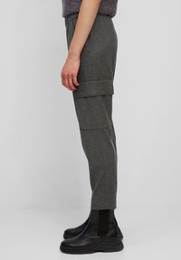 Grijze op maat gemaakte broek met een platte tailleband, voorzien van zijzakken en een omgeslagen zoom. Gepaard met zwarte enkelboots, lijkt de stof gestructureerd.