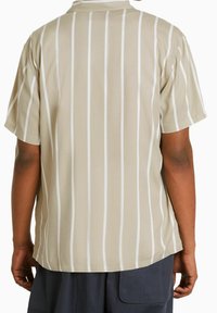 Vaaleanbeige lyhythihainen paita, jossa on pystysuoria valkoisia raitoja, klassisella kauluksella ja rentolla leikkauksella. Sileä kangas.