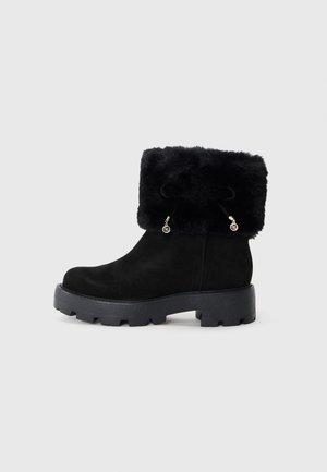 Zwarte enkellaarsjes van suede met een kunstbont manchet. Voorzien van een dikke, gestructureerde zwarte zool en decoratief koord met metalen accenten.