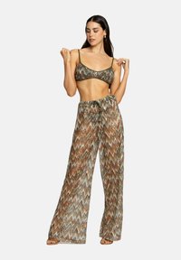 Set di top bikini a zigzag multicolore e pantaloni a gamba larga in tessuto trasparente; tonalità terrose di verde, marrone e crema.