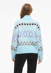 Hellblauer Pullover mit geometrischen Mustern in dunklerem Blau, Schwarz und cremefarbenen Akzenten; weiche Textur mit hohem Kragen.