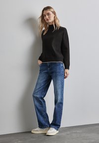 Maglione nero a maglia con collo alto e orlo a costine, abbinato a jeans blu a gamba dritta e sneakers chiare. Dettagli in tessuto testurizzato.