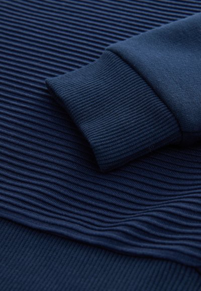 Tumši zila teksturēta sporta džempera ar vertikālām ribām un gludu aproces detaļu. Audums izskatās mīksts, kas norāda uz potenciālu komfortu.