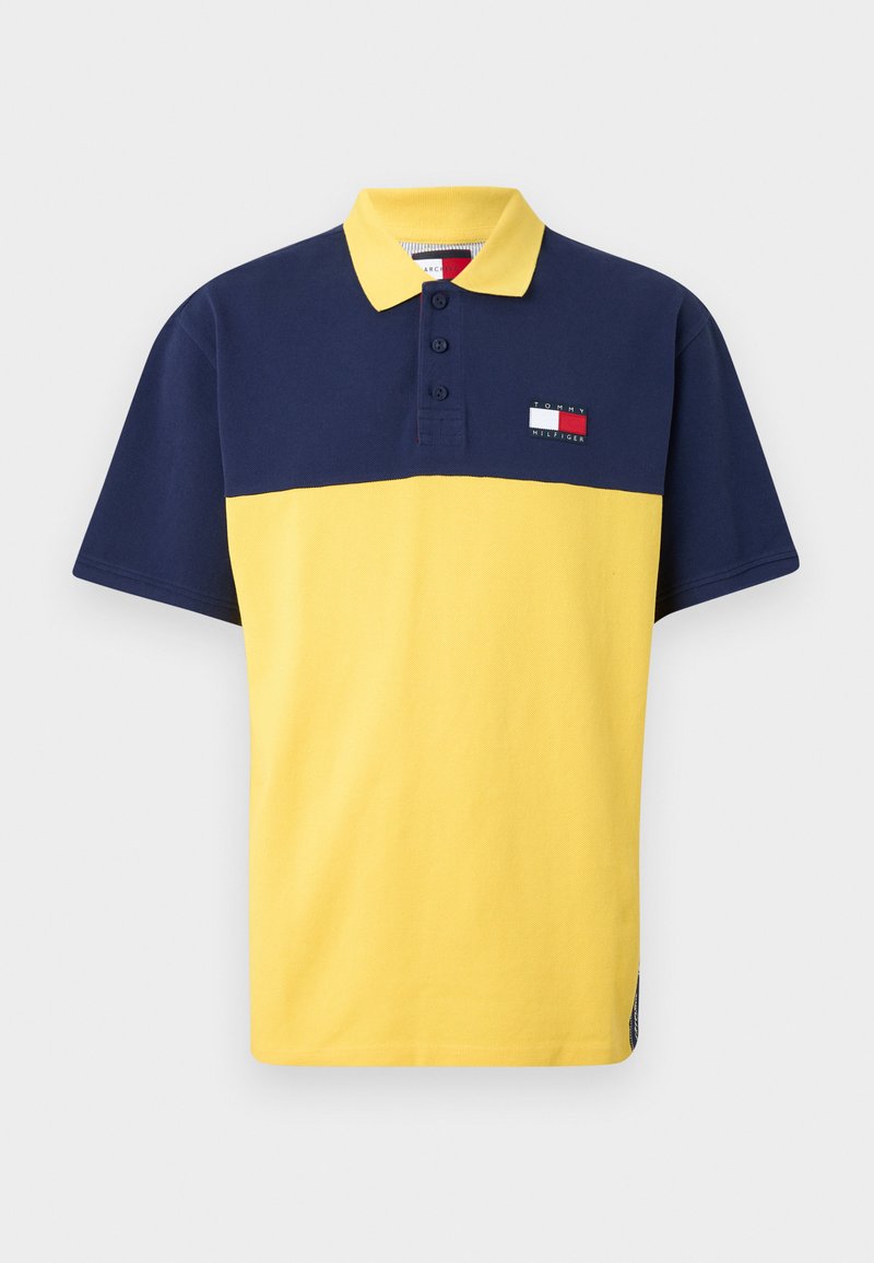 Polo Tommy Hilfiger avec une moitié supérieure bleu marine et une moitié inférieure jaune, doté d'une patte de boutonnage à trois boutons et d'une écusson logo sur la poitrine.