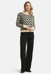 Knitted sweater in cream with black zigzag pattern, featuring long sleeves and a soft, fuzzy texture. Paired with black, tailored pants.