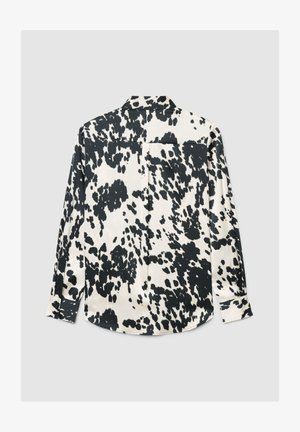 Langärmliges Hemd mit Knopfleiste und schwarz-weißem Kuhfleckenmuster, flach auf hellgrauem Hintergrund liegend, Rückseite gezeigt.