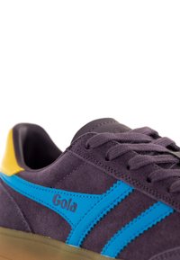 Purple suede sneaker with blue and yellow accents. Features a textured finish, lace-up closure, and "Gola" logo on the side.