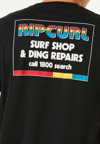 Sort T-shirt med et farverigt grafik på ryggen, der står "RIPCURL" med fede bogstaver i røde, blå og gule nuancer, samt reparationsdetaljer nedenfor.