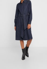 Jeansklänning i mörkblått med knäppning fram, långa ärmar och knytning i midjan. Matchad med svarta spetsiga ankelstövlar.