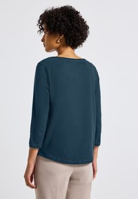 Ciemnoniebieska bluzka z długim rękawem, okrągłym dekoltem i miękkim, teksturowanym materiałem, cechująca się luźnym krojem i subtelnymi detalami szwów.