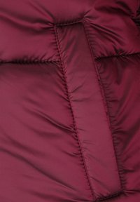 Bordó légpárnás dzseki részlet, sima, fényes felülettel, vízszintes steppelési vonalakkal és függőleges varrási részlettel.