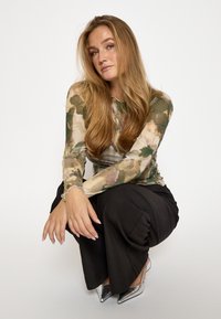 Garās piedurknes, caurspīdīgs tops ar zaļu un bēšu ziedu rakstu, kombinēts ar brīvām melnām biksēm un sudrabainām augstpapēžu kurpēm.