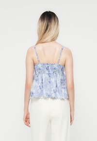 Bloemmotief top in lichtblauw met dunne bandjes, smock bodice en een vloeiende zoom. De stof heeft een zachte textuur en golvende randen.