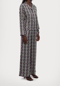 Ensemble de pyjama à motif noir et blanc avec des dessins floraux roses ; chemise à manches longues et pantalon ample, fabriqués en tissu doux.