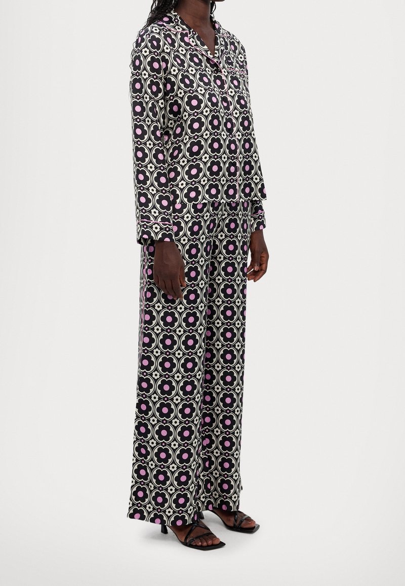 Ensemble de pyjama à motif noir et blanc avec des dessins floraux roses ; chemise à manches longues et pantalon ample, fabriqués en tissu doux.
