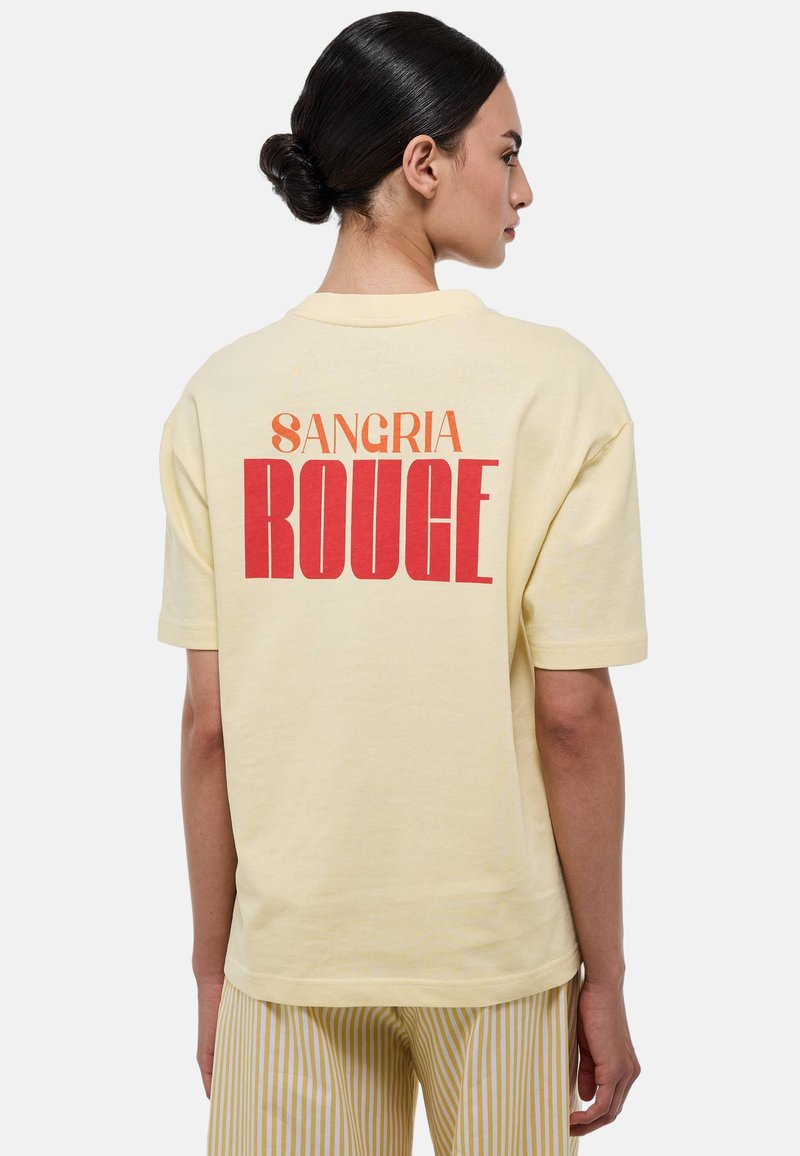 T-shirt en coton jaune avec le texte audacieux en rouge et orange "SANGRIA ROUGE" dans le dos. Manches courtes, coupe décontractée, texture douce.