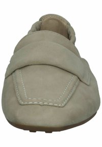 Chaussure en daim beige clair à enfiler, avec une large bride incurvée sur le dessus et des coutures blanches le long du bord. Design à bout arrondi.