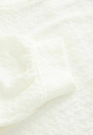 Bílá texturovaná látka s jemně mačkaným povrchem, obsahující detail s nařaseným manžetou. Materiál se zdá být lehký a měkký.
