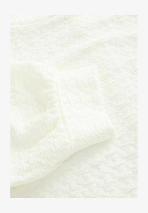 Valge tekstureeritud kangas kortsulise viimistlusega, millel on kogutud mansetid. Materjal paistab kerge ja pehme.