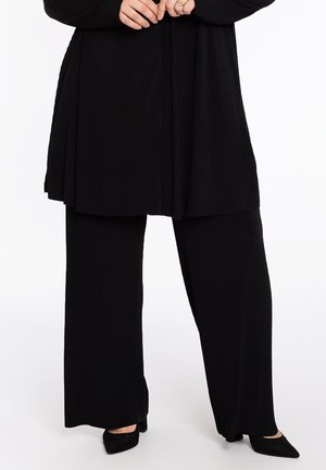 Zwart geribbeld tuniek met een vloeiende stijl gecombineerd met zwarte wijde broek. Beide stukken hebben een gestructureerde stof en subtiele beweging.