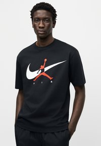 Μαύρο βαμβακερό t-shirt με στρογγυλή λαιμόκοψη, με μεγάλο λευκό και κόκκινο λογότυπο Jumpman και το κείμενο "AIR" από κάτω. Λεία υφή, άνετη εφαρμογή.