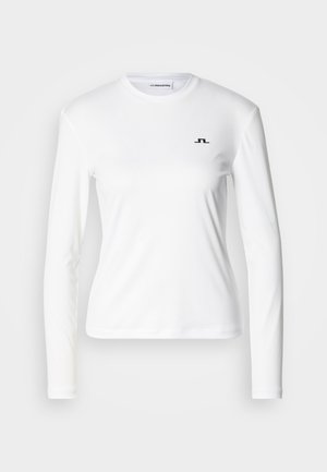 Chemise blanche à manches longues en tissu lisse, arborant un logo noir sur la poitrine, col rond et coupe ajustée.