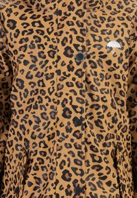 Leopárdmintás esőkabát bézs háttérrel, fekete és barna foltokkal, patentos záródással és kis fehér ernyőlogóval a mellkason.