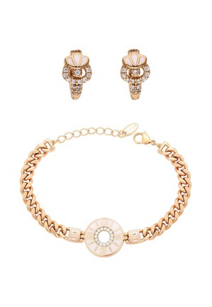 Złota bransoletka łańcuszkowa z okrągłym białym centrum ozdobionym cyrkoniami i rzymskimi cyframi, zestawiona z dopasowanymi złotymi kolczykami z cyrkoniami i białą muszlą.