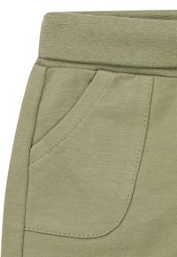 Licht olijfgroen stof met ribbelstructuur, voorzien van een zijzak en een elastische tailleband, zichtbare stiksels langs de randen.