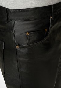 Zwarte leren broek met een gladde textuur, voorzien van gouden hardware accenten op de voorzakken en een klassieke vijfzakkenontwerp.