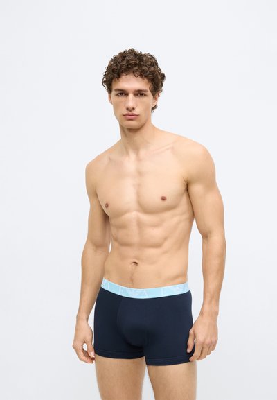 Tengerészkék boxeralsó világoskék elasztikus derékpánttal, amelyen logó található. Az anyag sima és rugalmasnak tűnik. Testhezálló kialakítás.