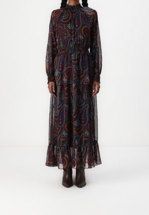 Personne portant une robe maxi noire à manches longues avec des motifs cachemire colorés et un ourlet à volants, associée à des bottines marron foncé.