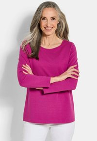 Langarm-Oberteil in Fuchsia aus weichem Stoff, mit Rundhalsausschnitt und lockerer Passform, kombiniert mit weißen Hosen.