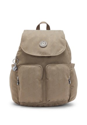 Beige fabric backpack with two front zip pockets, a top flap with a round metal logo, side pockets, and a keychain attached to one zipper.