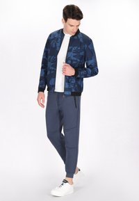 Marine bomberjack met geometrische patronen, geribbelde manchetten en een ritssluiting, gecombineerd met marineblauwe tapered joggers en witte sneakers.