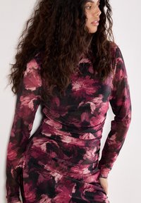 Langärmliges, florales Kleid in einer Mischung aus rosa und schwarzen Farbtönen. Der Stoff ist weich, hat eine figurbetonte Passform und Raffung an der Taille.