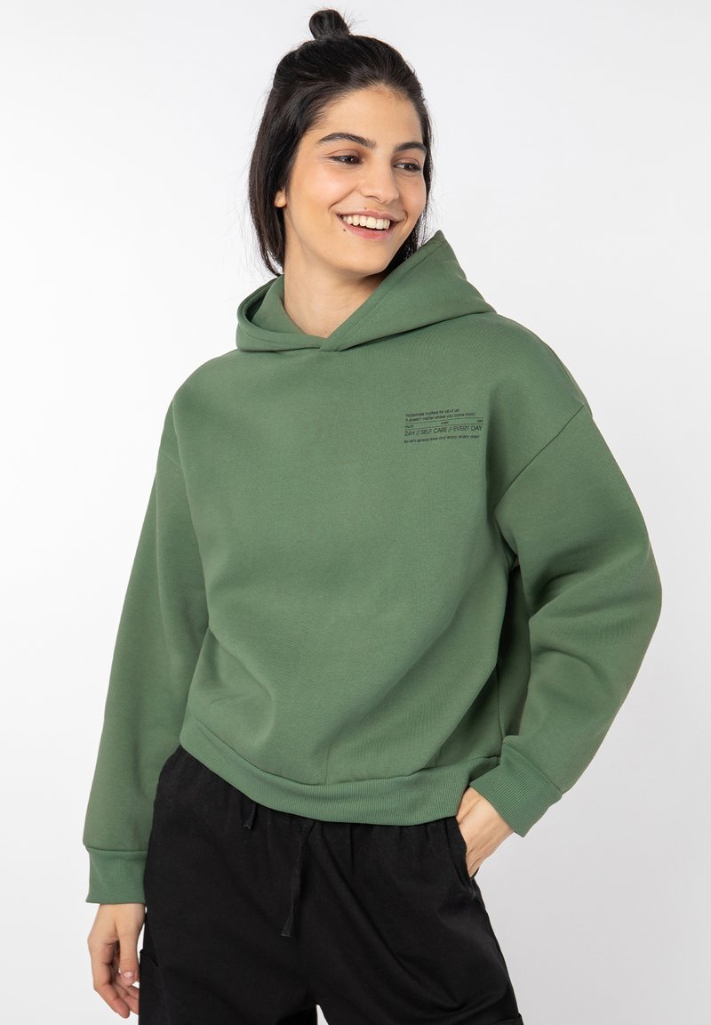 Loose-fitting green hoodie with a front pocket and print detailing. Soft fabric, long sleeves, and a drawstring hood for adjustability.