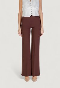 Pantaloni marroni a palazzo aderenti con una texture liscia. Abbinati a una blusa bianca con pieghe e bottoni decorativi.