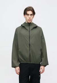 Ελαφρύ τζάκετ σε ελαιόχρωμο με κουκούλα, μπροστινό φερμουάρ, ελαστική μέση και μακριά μανίκια, φτιαγμένο από απαλό ύφασμα με ματ υφή.