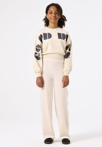 Crèmekleurig sweatshirt met gedurfde zwart grafische patronen, gecombineerd met hoog-gesneden, geribbelde crèmekleurige broek en zwarte instapschoenen. Soepele textuur.