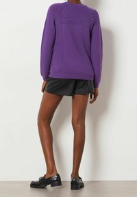 Paarse gebreide trui met geribbelde textuur op de schouders, ontspannen pasvorm, gecombineerd met zwarte shorts en zwarte chunky schoenen.