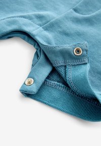 Niebieska bawełniana tkanina o gładkiej fakturze, z wzmocnioną krawędzią i metalowym zatrzaskiem na dolnym brzegu.