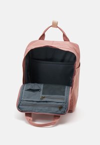 Różowy materiałowy plecak z zamkiem błyskawicznym, z pojemnym wnętrzem oraz szarym wypinanym modułem z kieszeniami z siateczki i zamkiem.