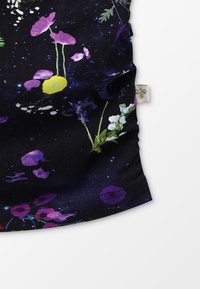 Blommönstrat tyg med mörk bakgrund, med lila, gula och gröna blommor; slät textur; fåll och etikett synliga.